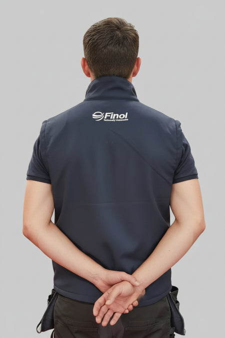 A man viewed from behind wearing a navy blue Finol insulated vest with a white logo on the upper back, standing in what appears to be a retail or workshop environment.